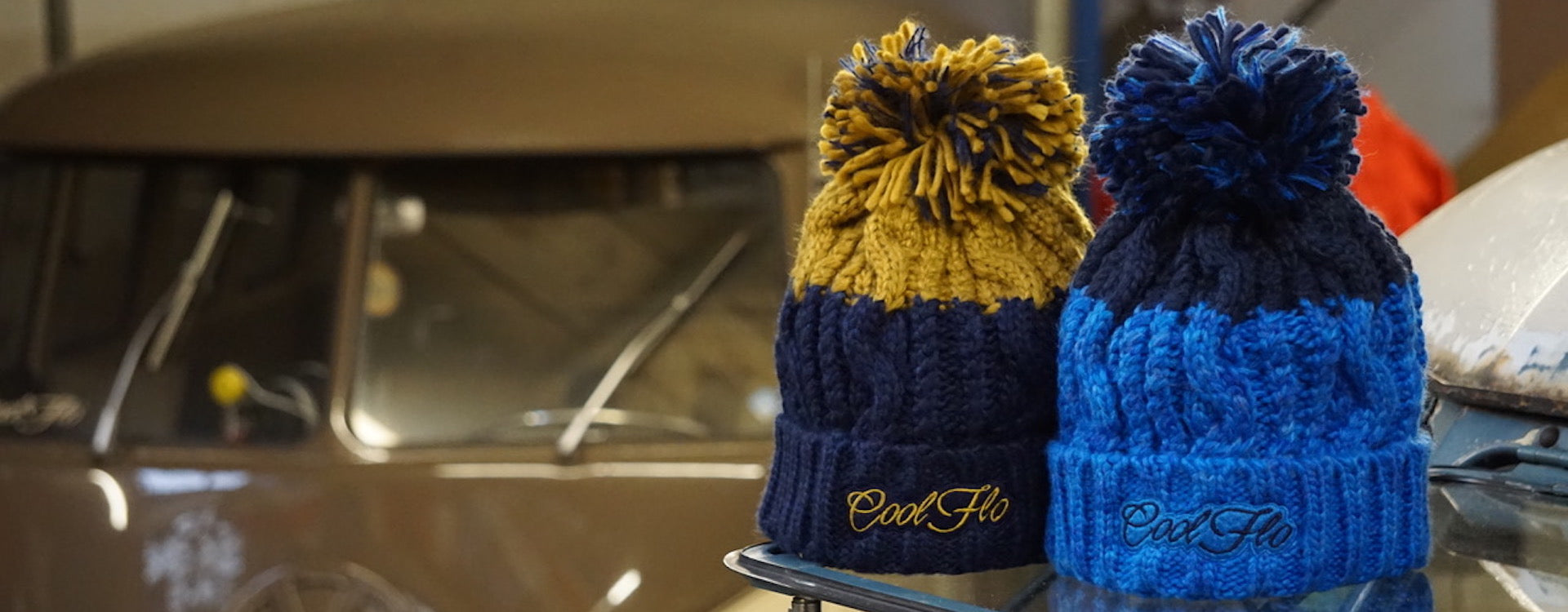 Two Cool Flo winter bobble hats sitting on an open VW campervan safari window with a VW bus in the background.