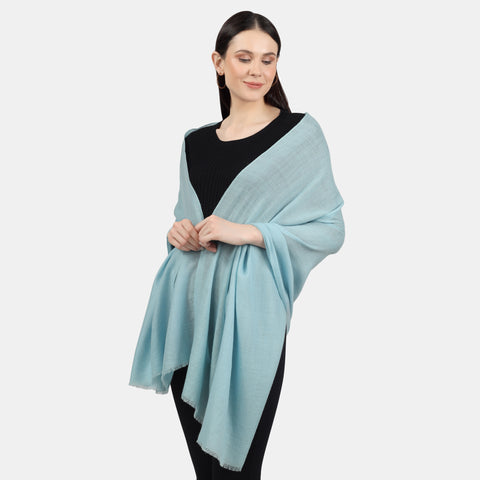 An image of a model wearing a black outfit accessorized with a Turquoise Cashmere scarf draped over her shoulders like a shawl wrap. The luxurious texture and vibrant color of the scarf bring a touch of elegance and warmth to the outfit, creating a fashionable and stylish look.