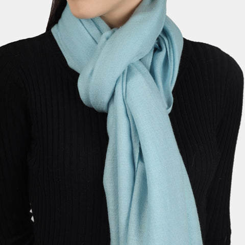 A photo of a model wearing a black outfit with a Turquoise Cashmere scarf tied in a knot around her neck. The scarf's bold turquoise color adds a pop of vibrancy to the monochromatic outfit, while the cashmere material provides a soft and cozy touch to the overall look.