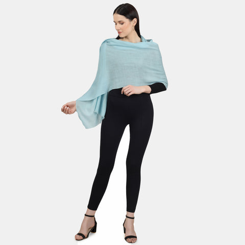 A fashion model wears a black outfit complemented by a beautiful Turquoise Cashmere scarf draped over her shoulders as a shawl wrap. The scarf's soft and cozy texture and the striking turquoise color contrast perfectly with the black outfit, creating a chic and sophisticated ensemble.