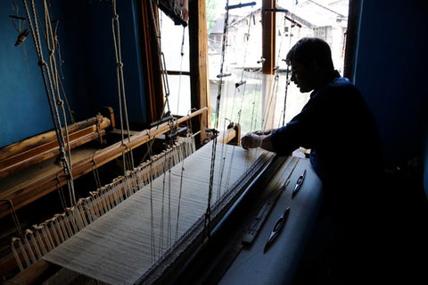 An artisan of Kashmir Weaving Cashmere yarn into a piece of cloth to make scarves and wraps on a wooden handloom in his home