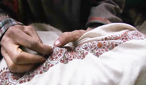 Image capturing a man's skilled hands engaged in Sozni hand embroidery, delicately working a needle on a Pashmina shawl to create intricate patterns.