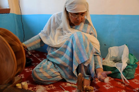 An elderly woman spinning fine Cashmere fibers into yarn on a traditional spinning wheel.