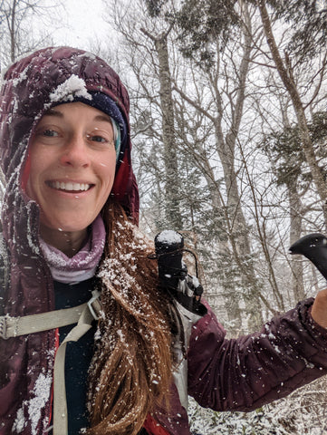 A female hiker is smiling as the snow falls around her