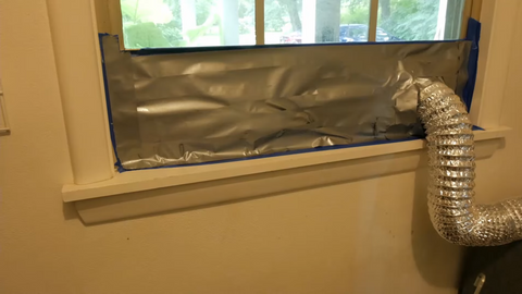 a large ventilation tube going through a window which is half sealed off with duct tape