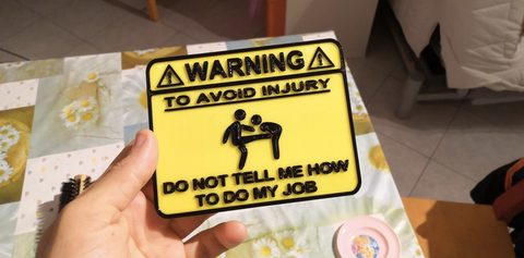 3D printed sign of a stickman kicking another stickman in the genitals. The sign reads "Warning. To avoid injury, do not tell me how to do my job"