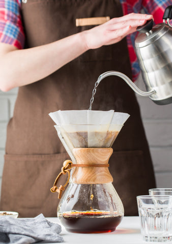 barista pours hot water from a gooseneck kettle into a Chemex to brew coffee