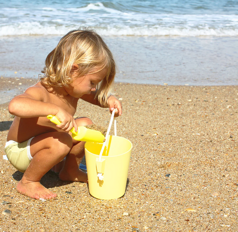 Child scooping sand in a beach bucket by Sunnylife