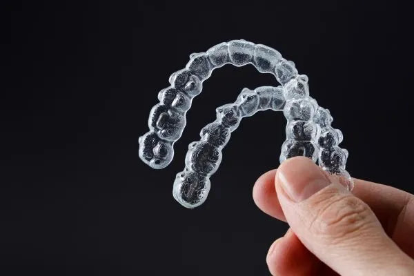 A hand holding two clear aligners