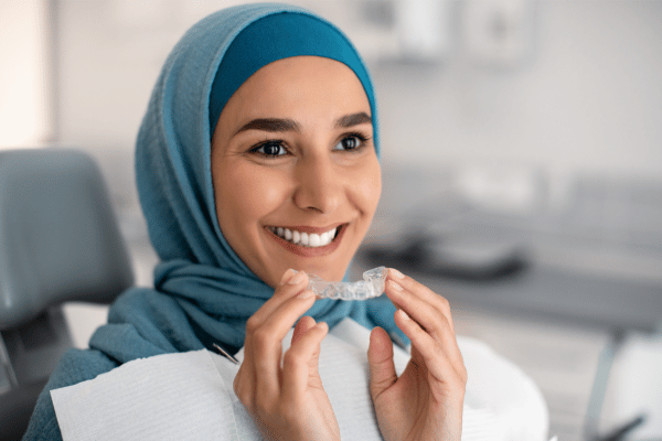 A woman smiling confidently holding clear aligners