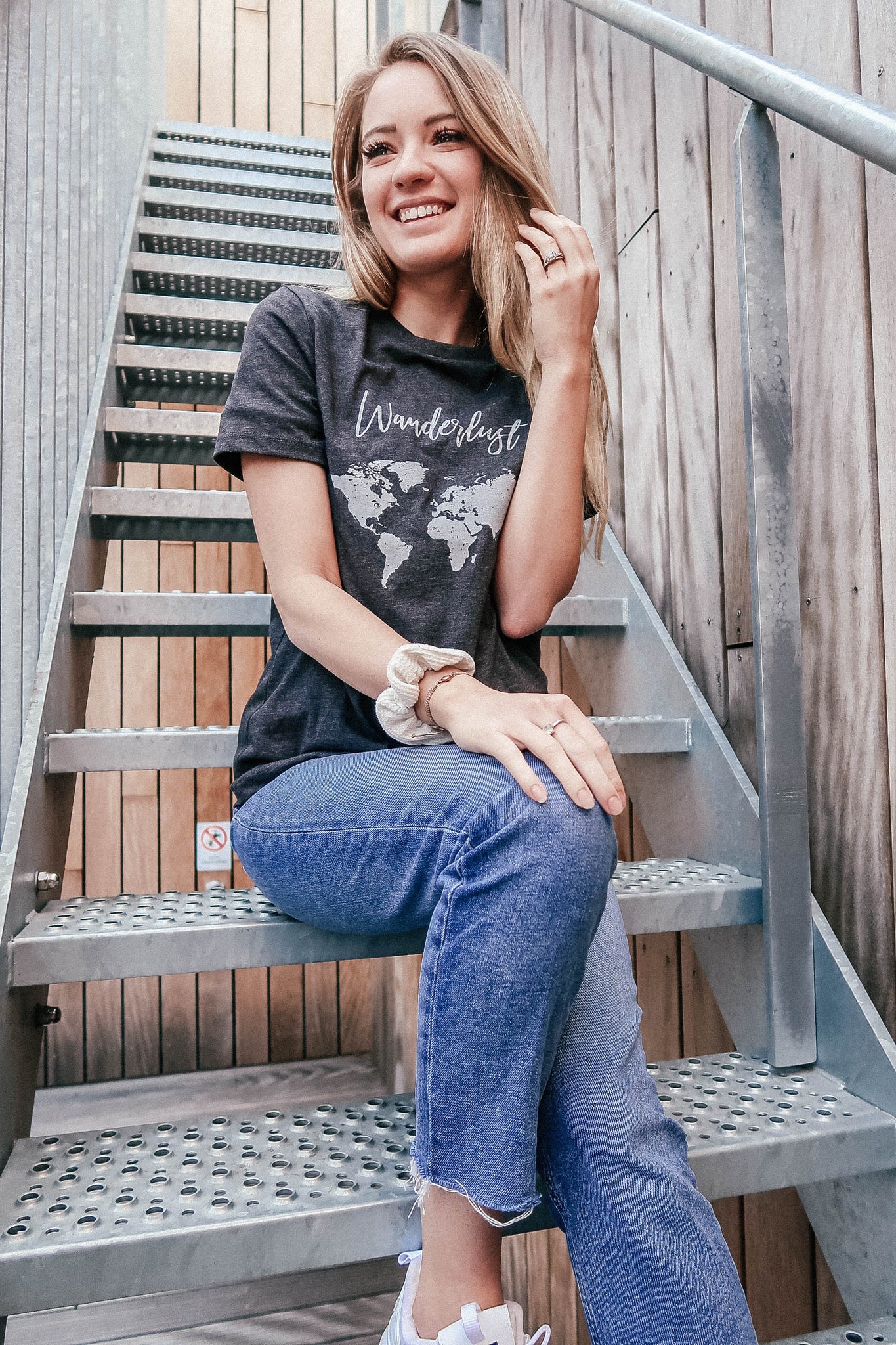 Meghan Knudson Female Wearing Wanderlust Travel Charcoal Relaxed Tee Sitting On Staircase