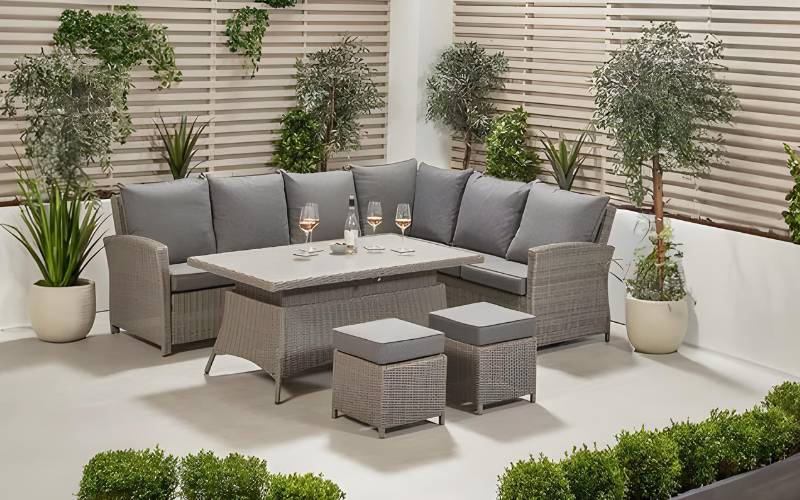 Slate Grey Barbados Corner Set Long Left with Ceramic Top arranged in an outdoor space, featuring a corner sofa, adjustable table, and two footstools, with potted plants and greenery in the background.