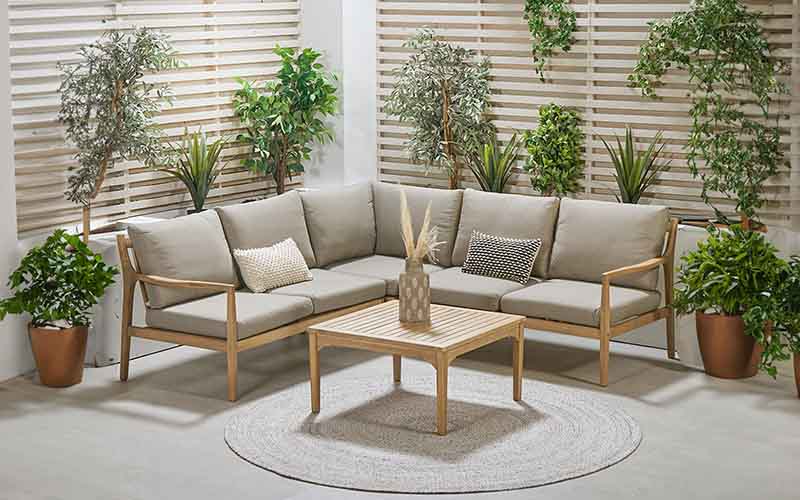 Malta Outdoor Corner Seating Set displayed in an indoor setting with decorative plants and a wooden coffee table.