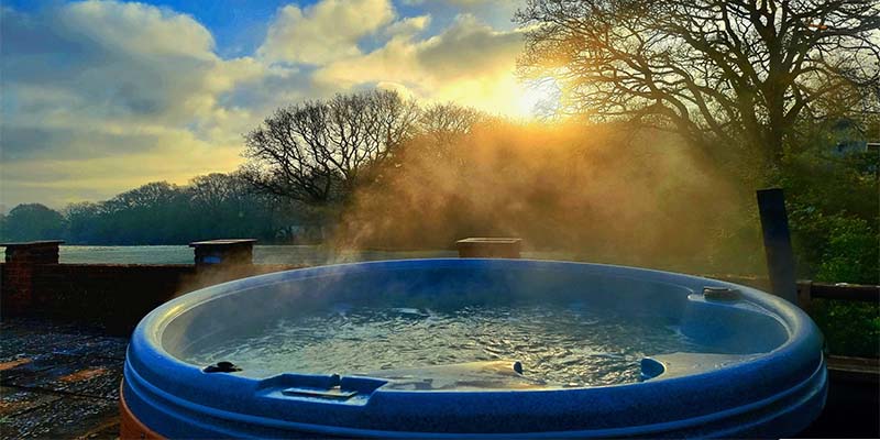 RotoSpa hot tub outdoors at sunrise with steam rising, front view.