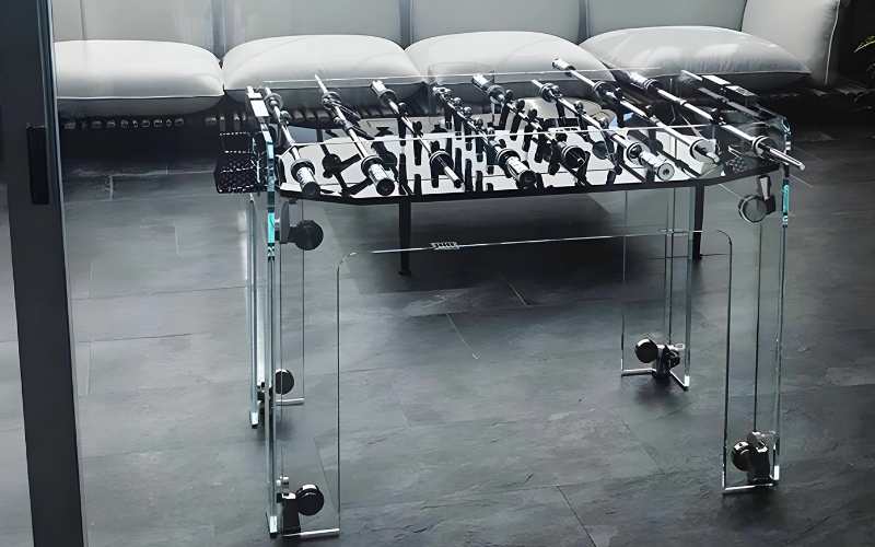 Teckell Cristallino Black Foosball Table in a modern living room setting with a sleek sofa in the background.