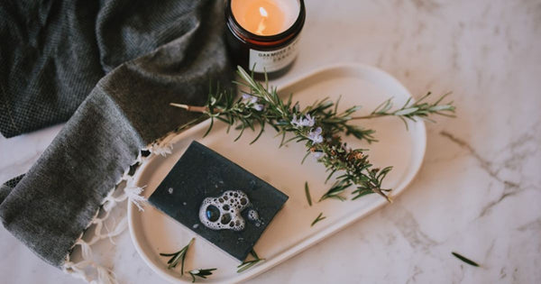 A handmade soap bar on a tray, next to a candle and fresh herbs
