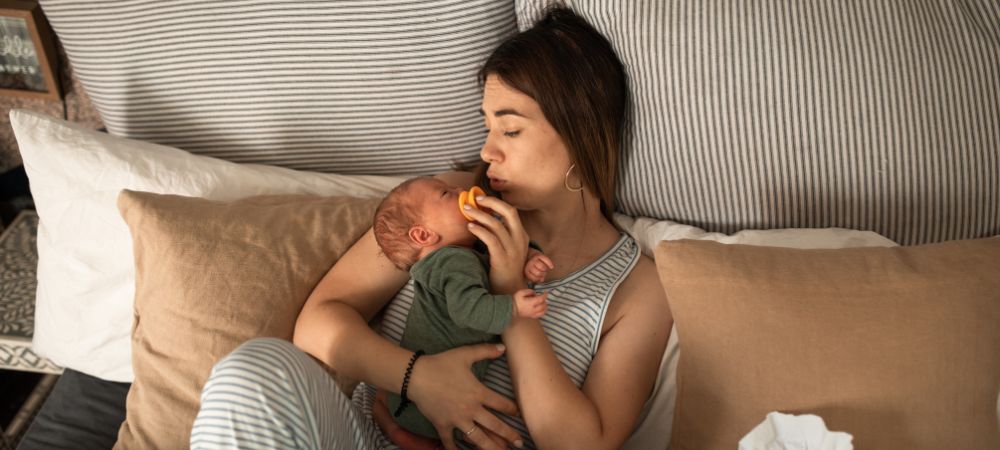 Mother in bed offering her newborn baby a pacifier 