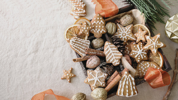 This is a flat-lay photo taken of Holiday cookies such as gingerbread people, sugar cookies, and snowflakes in a box with ribbon and pine surrounding the box