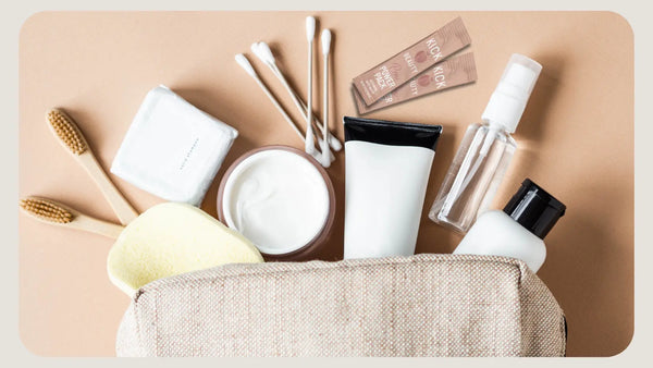 Flat lay image of a toiletry bag with common skincare items for travel displayed.  Items include shampoo, toothbrush, cotton swabs, lotion, and PM POWER PACK by KICK PEACH BEAUTY