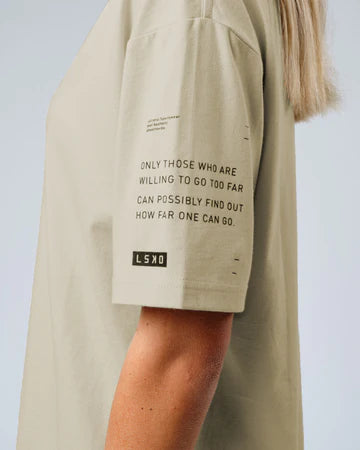 Female model wears LSKD oversize tee in taupe. Image shoes sleeve detailing with LSKD logo