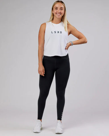 Female model wears LSKD rep tank in white and deep teal. Paired with black leggings and white trainers.