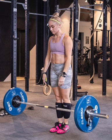 Athlete waering the new WIT square neck elderberry bar with a barbell in front of them. Hairstyle is a bun with a yellow headband