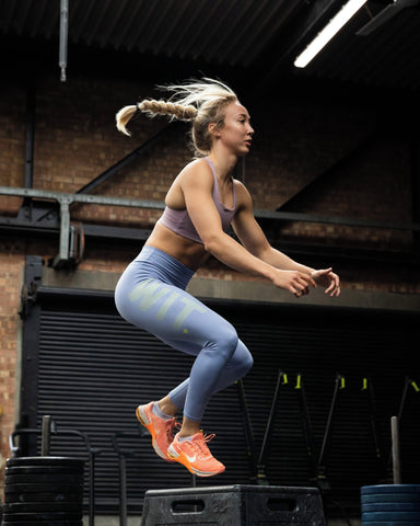 Model is mid box jump with a single braid, wearing the new WIT soft legging and comp bra combo in purple