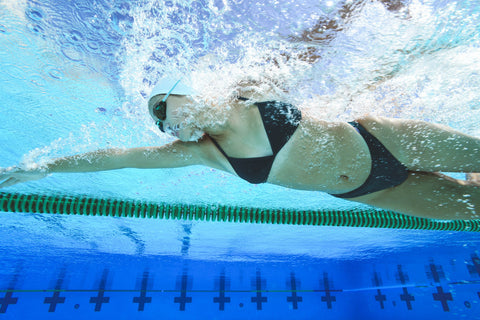 Žena v černých bikinách plave v bazénu.