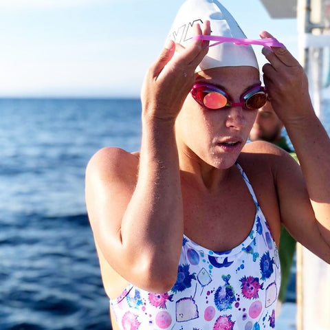 Sportliche Schwimmerin in Badeanzug setzt sich eine weiße Schwimmkappe mit rosa Streifen auf.