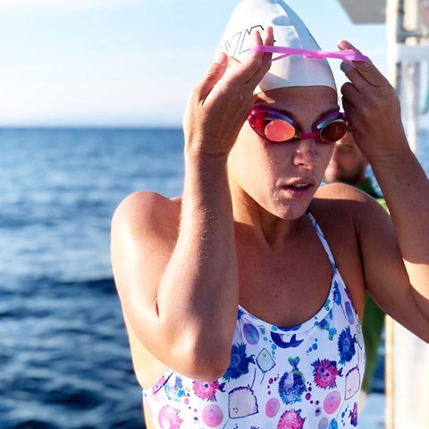 Female swimmer in swimming costume with pink stripes and red swimming goggles.