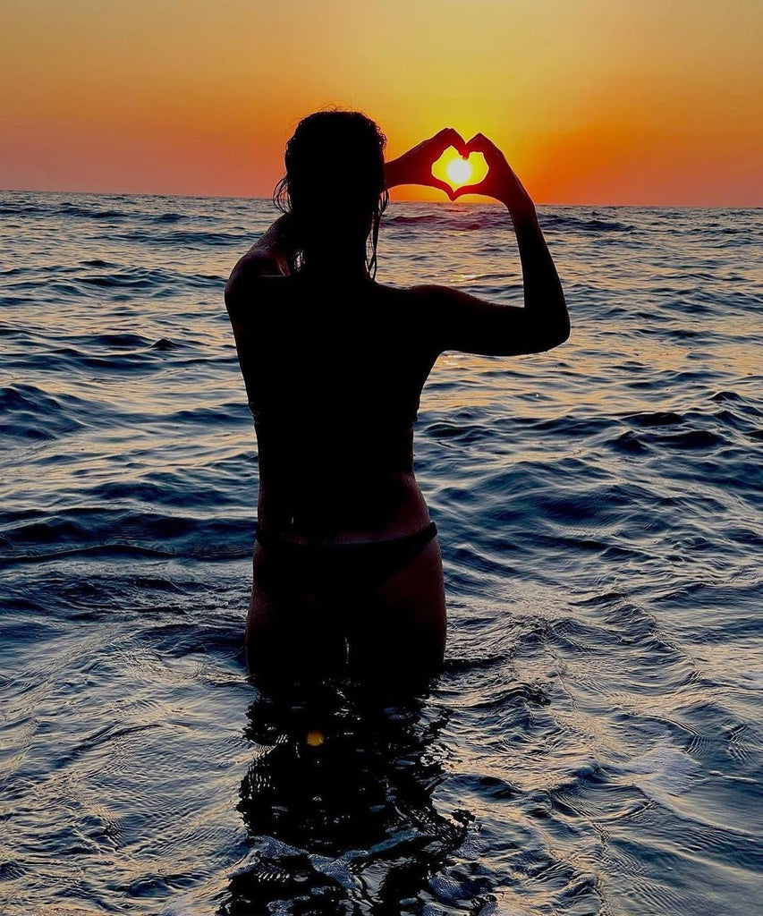 Woman with bikini in the sea shows a heart