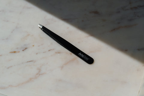 ArteStile Slant Tip Tweezer in Matte Black. Tweezer is on a marble table top.