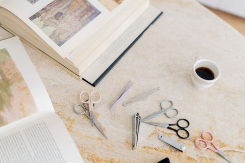 ArteStile brow scissors and tweezers on a table with photo books and a cup of coffee