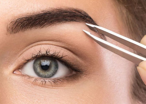 Image of a women plucking a hair out of her brow with tweezers 