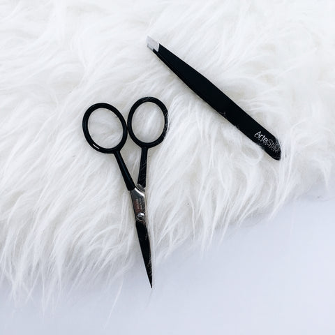 A pair of black scissors and a pair of black tweezers on a white, fluffy background.