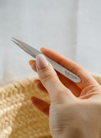 A hand holding the ArteStil point tip tweezers. The tweezers are entirely stainless steel with a sharp point for precision tweezing.