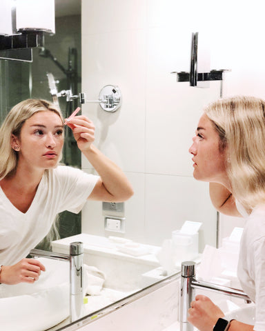 woman in front of mirror tweezing her brows