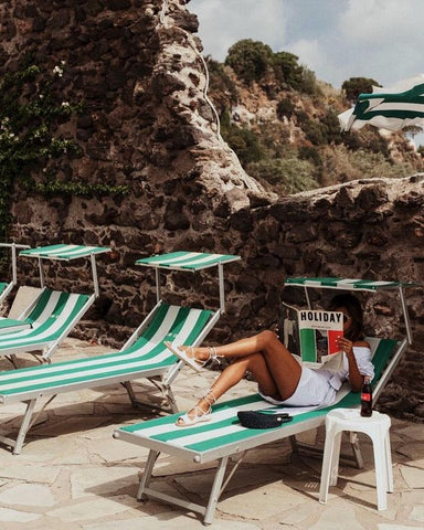 woman sitting on chair on beach in Italy reading a magazine