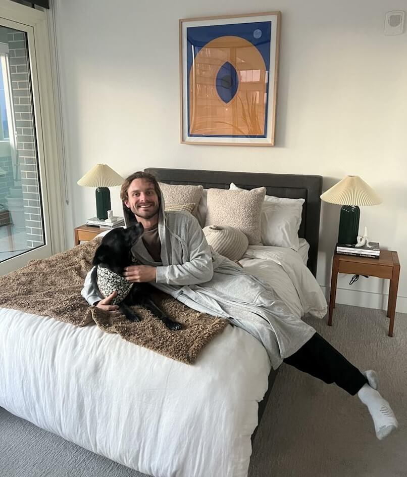Person relaxing on a bed with a dog in a cozy bedroom setting.