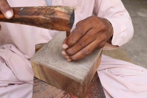 an artisan is ethically wood carving a block print block for natural dyeing