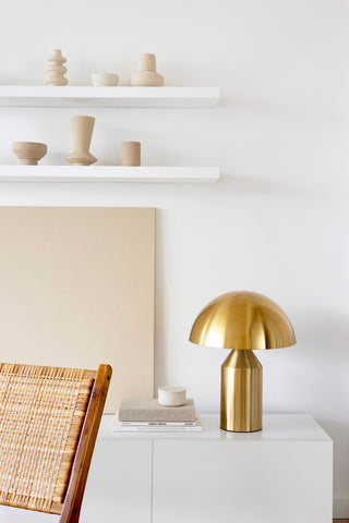 vases en céramique beige sur étagères murales blanches avec lampe champignon en laiton sur console avec livres et chaise en rotin