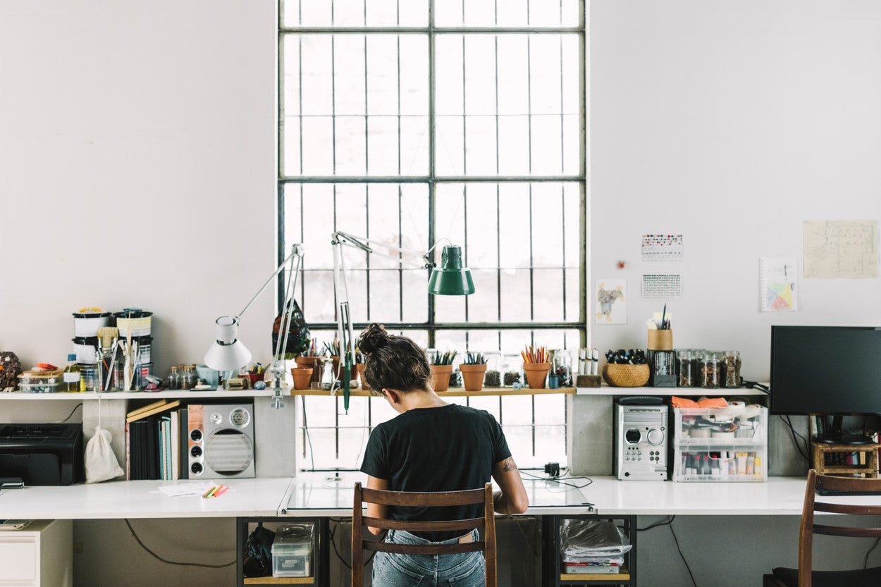 Woman working at a wide desk filled with art supplies