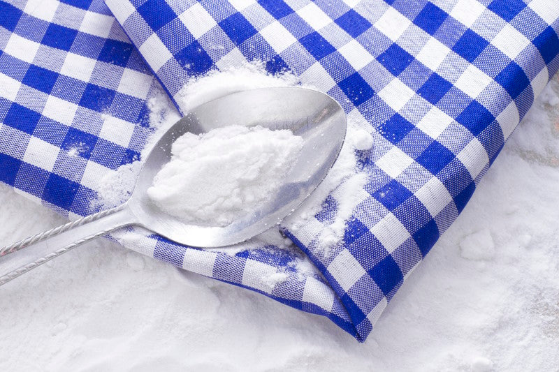 Spoon full of baking soda on top of a blue gingham cloth
