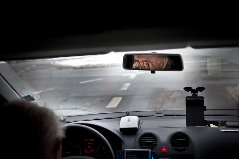View from backseat of driver rubbing eyes in rearview mirror
