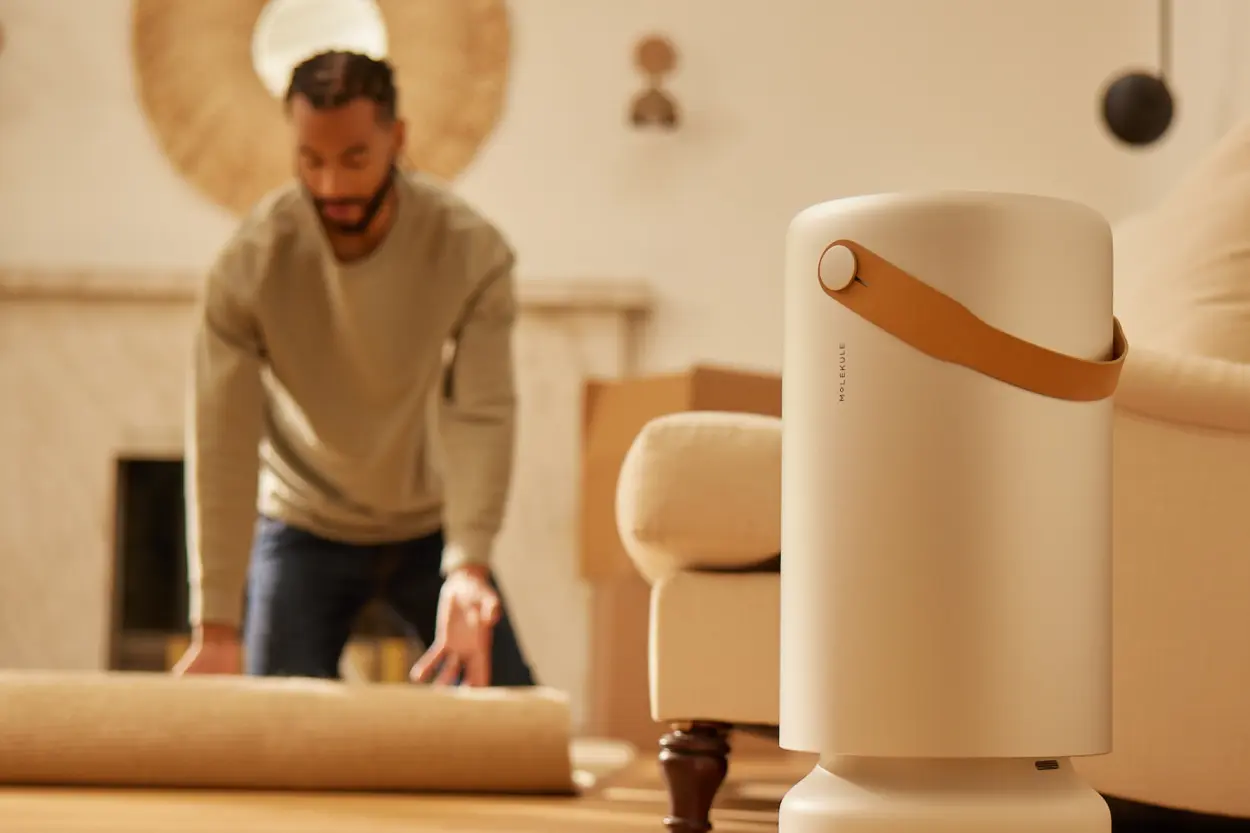 Man unrolling a new rug while a Molekule Air Pro purifies the air nearby.