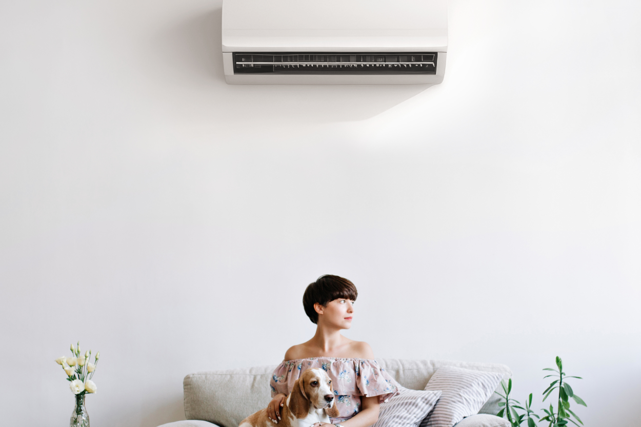 Woman with dog sitting below ductless HVAC mini split system enjoying cool air.