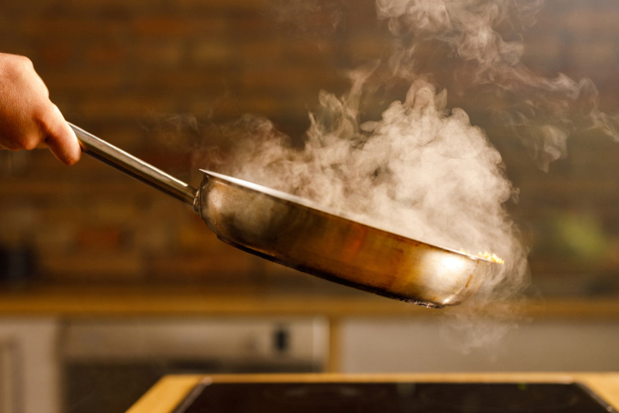 Person handling a steaming frying pan over the stove