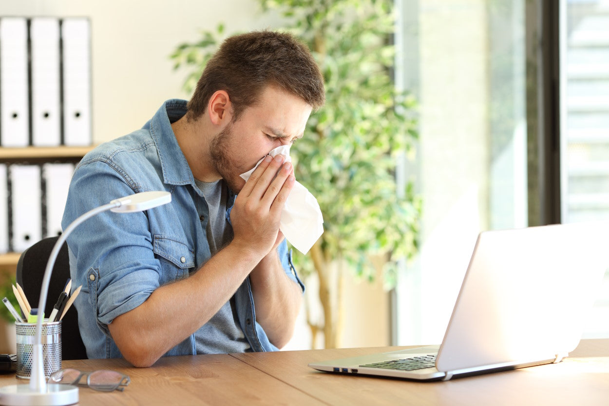 Man blowing his nose at office desk