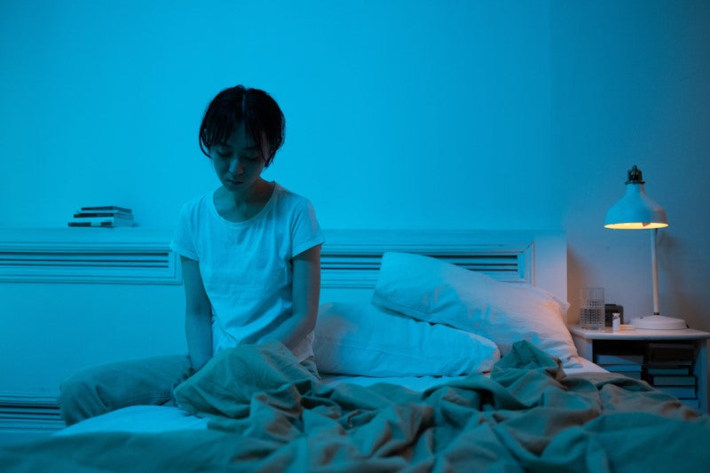 Sad woman sitting on a bed with a blue filter