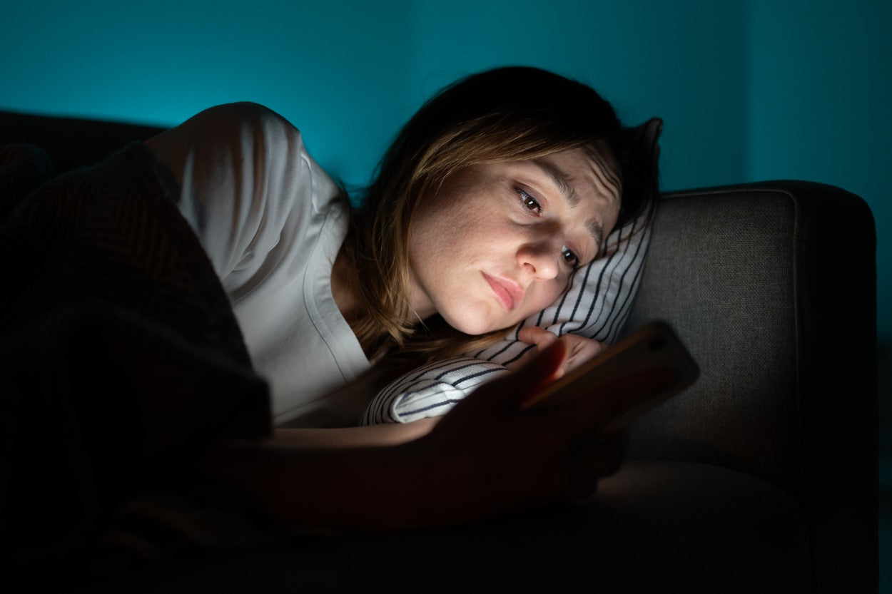 Unhappy woman lying on the couch and looking at cellphone